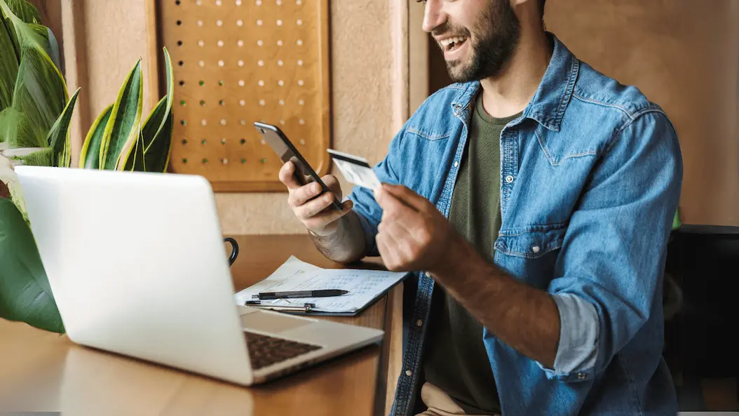 Hombre sonriendo mientras mira el celular y en su otra mano sostiene un celular